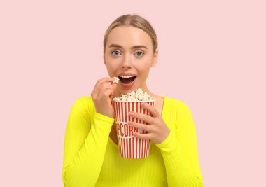 Mutlu genç bir kadın pembe arka planda patlamış mısır yiyor.