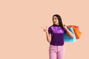 Güzel, mutlu, alışveriş çantalı genç bir kadın bej arka planda bir şeyi işaret ediyor.