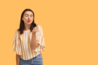 Güzel, genç, mutlu bir kadın sarı arka planda kalp hareketi gösteriyor.