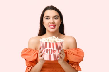 Pembe arka planda patlamış mısırı olan güzel, genç bir kadın.