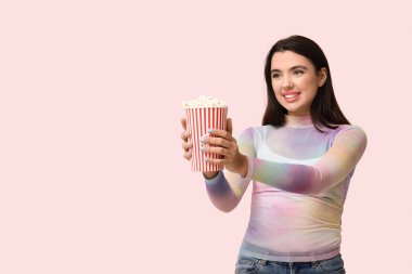 Pembe arka planda patlamış mısırı olan güzel, genç bir kadın.