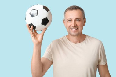 Mavi arka planda futbol topu olan yakışıklı olgun bir adam.