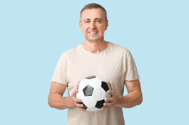 Mavi arka planda futbol topu olan yakışıklı olgun bir adam.