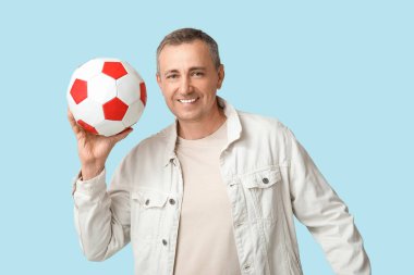 Mavi arka planda futbol topu olan yakışıklı olgun bir adam.