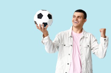 Mavi arka planda futbol topu olan yakışıklı genç adam.