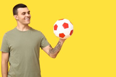 Sarı arka planda futbol topu olan yakışıklı genç adam.
