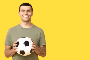 Sarı arka planda futbol topu olan yakışıklı genç adam.