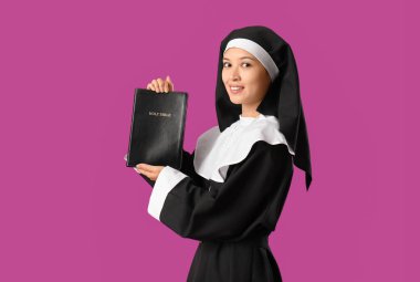 Mor arka planda İncil 'i olan güzel genç Asyalı rahibe.