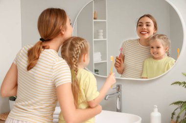 Genç anne ve küçük kızı banyoda aynanın yanında diş fırçaları ile