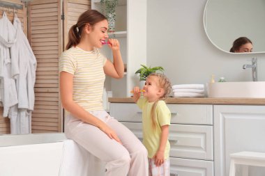Genç anne ve küçük kızı banyoda dişlerini fırçalıyorlar.