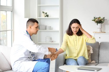 Erkek doktor evde genç bir kadının ateşini ölçüyor.