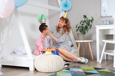 Süslü yatak odasında oturan küçük tatlı oğlu için doğum günü pastalı anne.