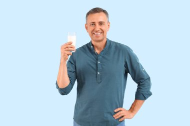 Mavi arka planda bir bardak sütle olgun bir adam.