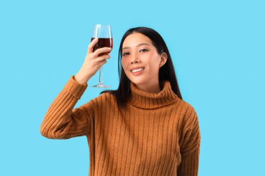 Mavi arka planda kırmızı şarap kadehi olan güzel Asyalı kadın.