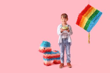 Pembe arka planda doğum günü pastası ve pinataları olan şirin bir çocuk.