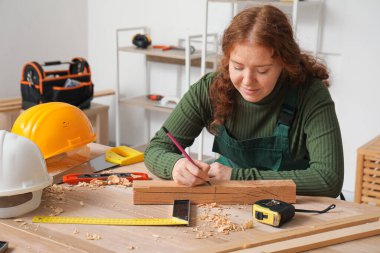 Dişi marangoz atölyede tahta kalemle işaretliyor.