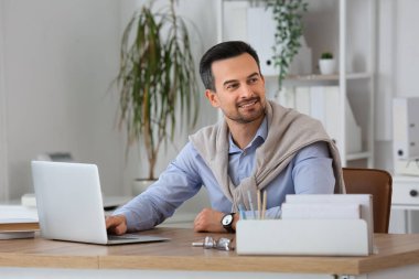Ofiste dizüstü bilgisayarla çalışan yakışıklı bir iş adamı.