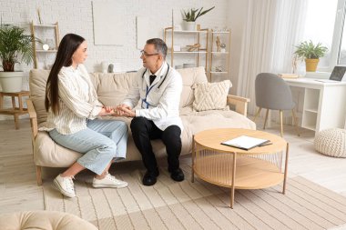 Evde hasta genç bir bayanın elini tutan olgun bir doktor.