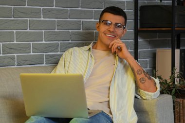 Erkek yazar evdeki koltukta dizüstü bilgisayar kullanıyor.