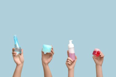 Mavi arka planda farklı kozmetik ürünleri olan kadın elleri