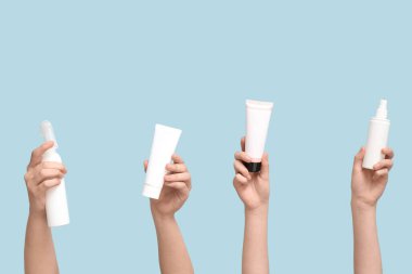 Mavi arka planda farklı kozmetik ürünleri olan kadın elleri