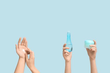 Mavi arka planda kozmetik ürünleri olan kadın elleri
