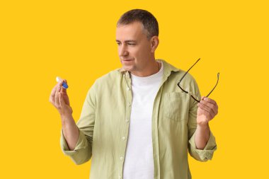 Lens kutusu ve sarı arka planda gözlüğü olan olgun bir adam.