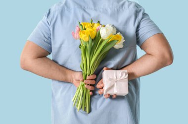 Hediye kutusu ve mavi arka planda bir buket güzel lalesi olan yakışıklı genç adam.