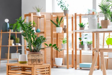 Çiçekçi dükkanındaki masada bitki ve sulama kutusuyla açık tabela