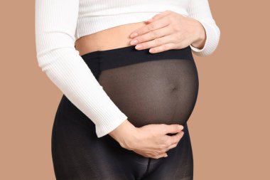 Siyah taytlı, bej arka planda hamile bir kadın, yakın plan.