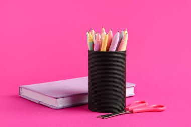 Pembe arka planda farklı kalem, defter ve makaslı tutucu