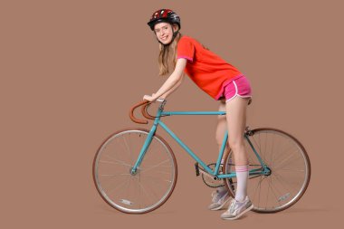Kasklı, kahverengi arka planda bisikleti olan güzel bir kadın.