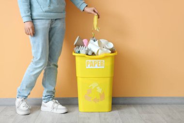 Bej duvarın yanında kağıt levhası olan çöp kutusuna çöp atan bir kadın. Geri dönüşüm kavramı