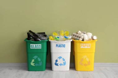 Yeşil duvarın yanında farklı çöp kutularıyla dolu çöp kutuları. Geri dönüşüm kavramı