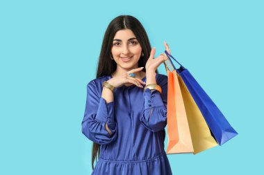 Mavi arka planda alışveriş torbaları olan güzel, genç, mutlu bir Hintli kadın.