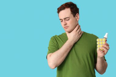 Boğazı ağrıyan genç bir adam, mavi arka planda haplar ve sprey