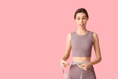 Güzel, genç, şok olmuş, pembe arka planda mezurası olan bir kadın.