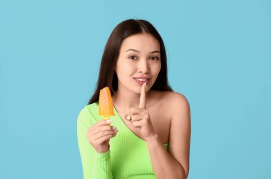 Mangolu güzel bir Asyalı kadın mavi arka planda sessizlik jesti yapıyor.