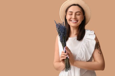 Bej arka planda bir demet lavanta çiçeğiyle güzel, mutlu genç bir kadın.