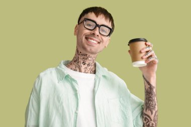 Yeşil arka planda kahve fincanı olan gözlüklü genç dövmeli adam.