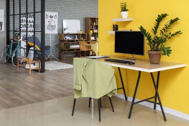 Ofiste sarı duvarın yanında bilgisayar monitörü ve bitkileri olan modern işyeri