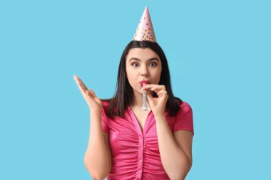 Mavi arka planda ıslık çalan parti şapkalı güzel bir genç kadın.