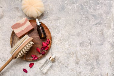Ahşap tepsi, vücut masajı fırçası, serum şişeleri, gül yaprakları ve grunge arkaplanda sabun kalıbı ile güzel bir kompozisyon.