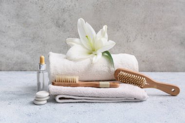 Bir şişe serum, spa taşları, zambak çiçeği, havlu ve masaj arka planda fırçalar.