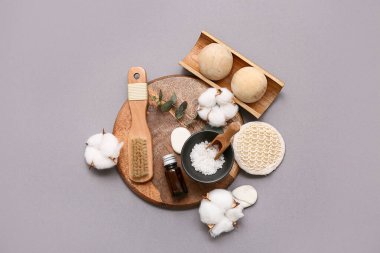 Ahşap tepsi, masaj vücut fırçası, deniz tuzu, pamuk çiçekleri ve gri arkaplanda okaliptüs dalı olan kompozisyon