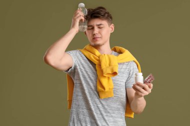 Yeşil arka planda baş ağrısından muzdarip bir şişe su ve haplı genç adam.