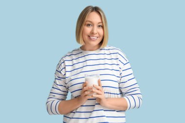 Mavi arka planda bir bardak taze sütle güzel genç bir kadın.