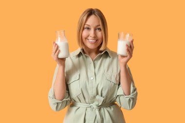 Sarı arka planda bardak ve bir şişe taze sütle güzel bir genç kadın.