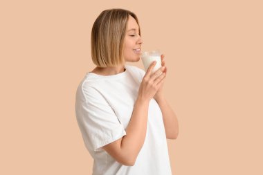 Güzel genç bayan bej arka planda taze süt içiyor.