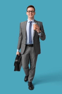 Elinde bir fincan taze kahve ve mavi arka planda evrak çantası olan yakışıklı bir genç.